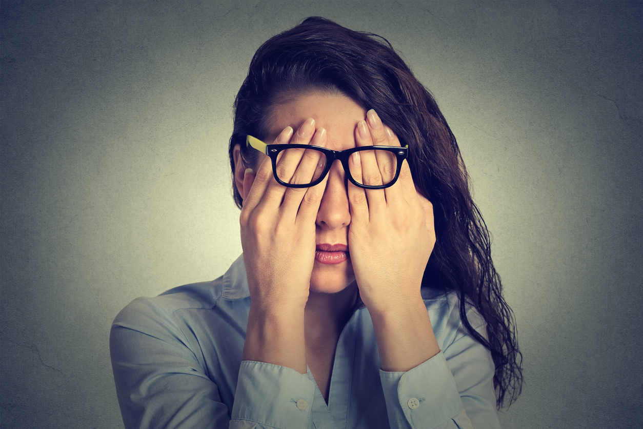 woman in glasses covering face eyes with two hands